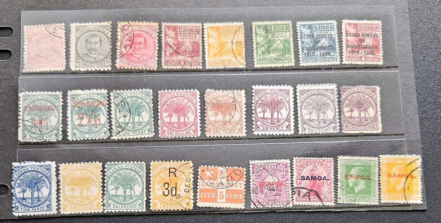 A collection of vintage Samoa postage stamps displayed in three horizontal rows on a clear plastic sleeve over a dark gray surface. The stamps feature various colors including green, pink, orange, blue, and yellow, with some showing cancellation marks.
