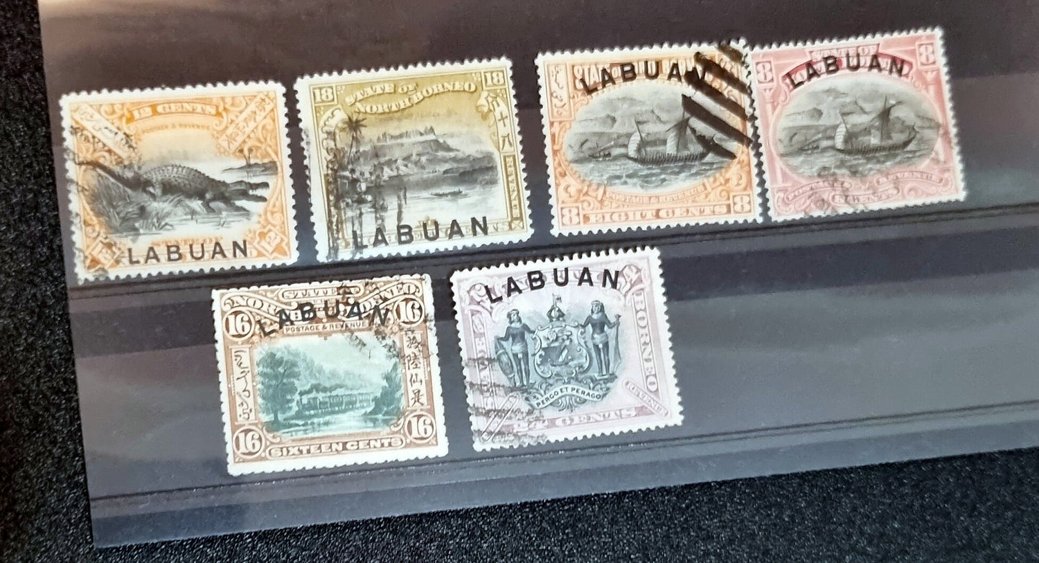A collection of six vintage Labuan postage stamps with various designs, predominantly in green, blue, and brown shades, featuring inscription &